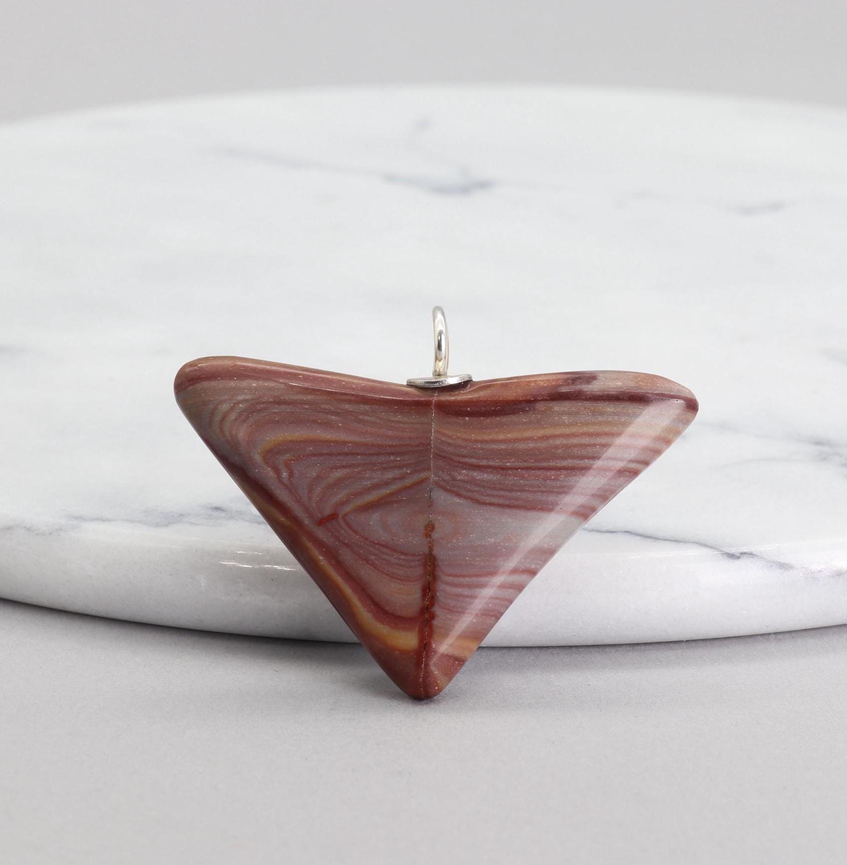 Front-facing view of this handcut polished Butterfly Shaped Petrified Rainbow Wood pendant featuring earthy tones of deep crimson, purple, and tangerine with handcrafted Argentium 935 silver bail shown against white marble slab and white background.
