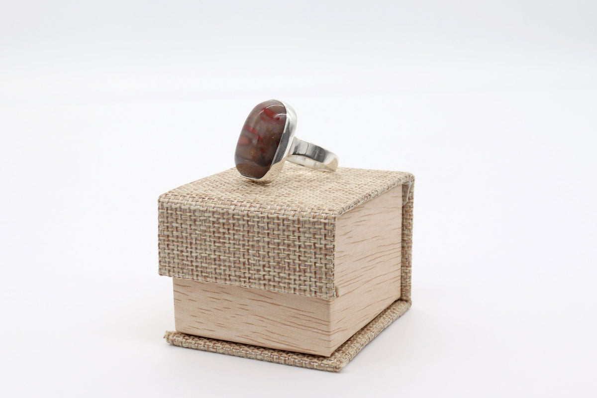 An Arizona Rainbow Petrified Wood ring handcrafted in Argentium 935 silver, displayed on top of a small wooden jewelry box against a white background.