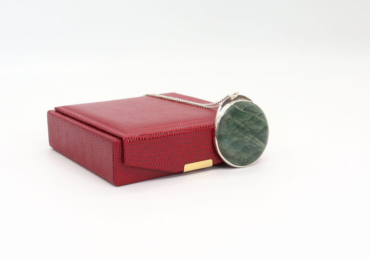 An Argentium silver chain and a round Arizona Lizard stone bezel pendant, shown next to its matching red textured presentation box on a white background.