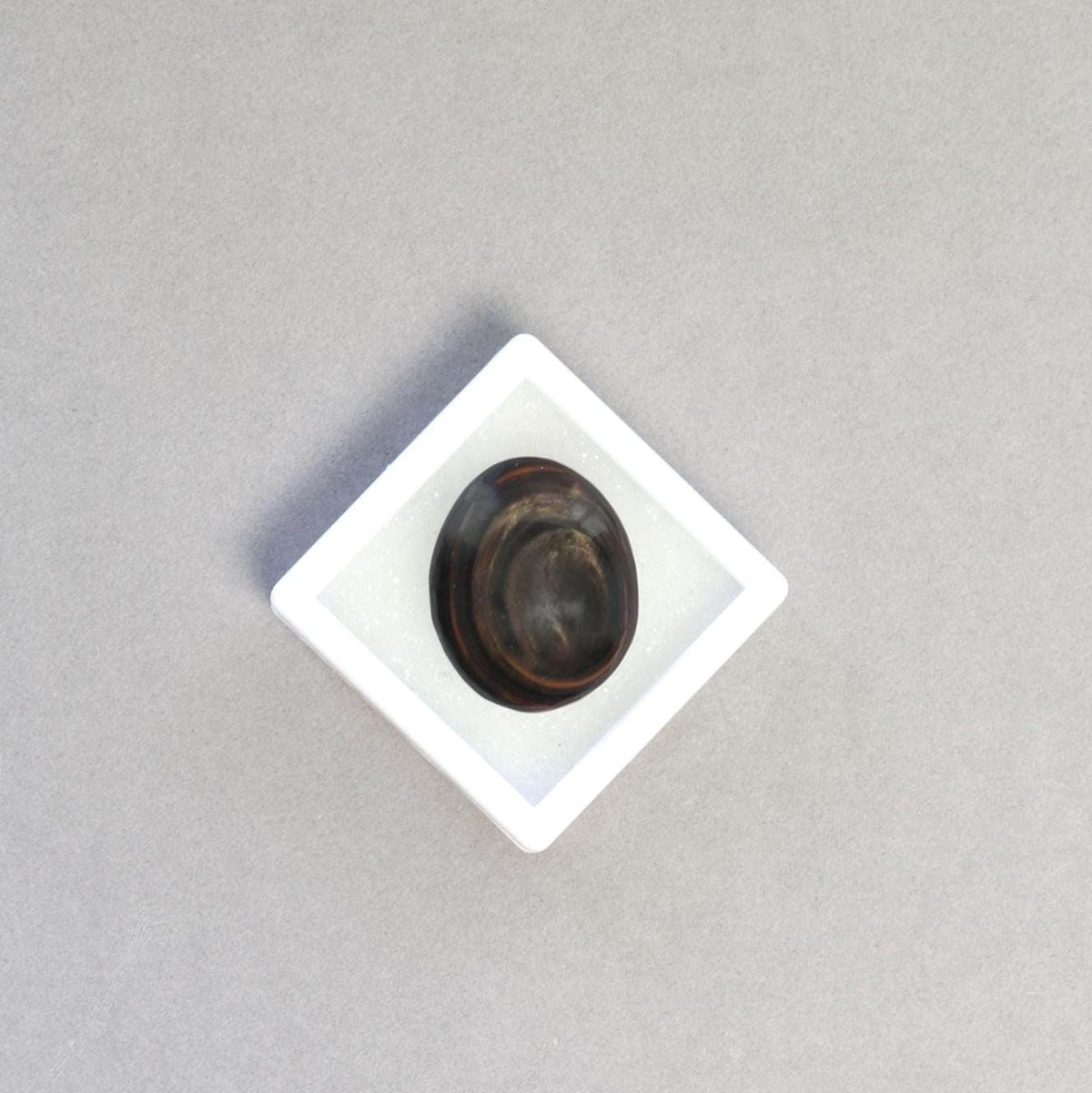 Mahogany Obsidian oval cabochon displayed in a white gem box shown on light gray background.
