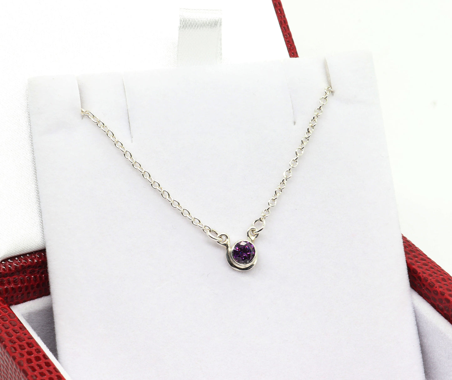 Purple Cubic Zirconia in Argentium Silver setting with attached argentium silver chain necklace links shown against white gift box.
