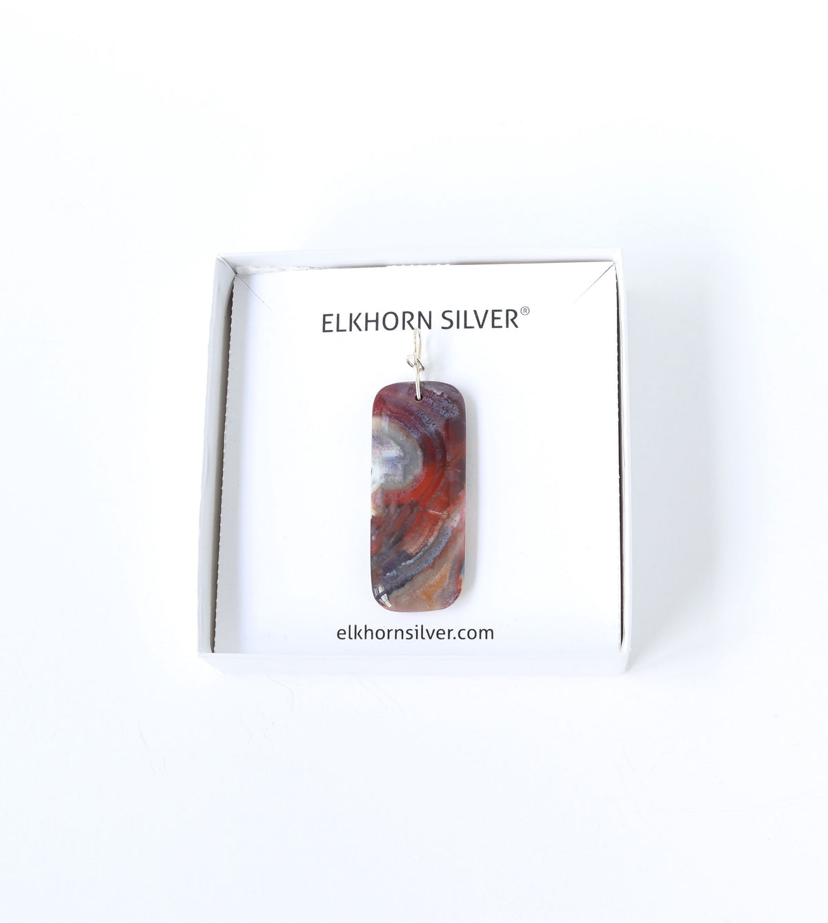 Pendant is shown in white gift box on white background. Pendant is a one-of-a-kind handcut and polished Red Mexico Agate (Natural Banded Agate) Pendant features flowing bands of deep red, purple, orange, black, and white.