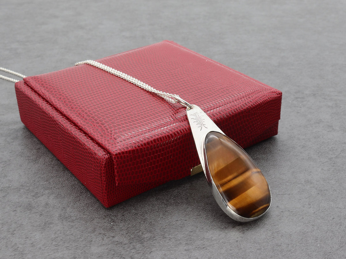 Tiger's eye teardrop pendant on a silver chain against a red gift box on gray background
