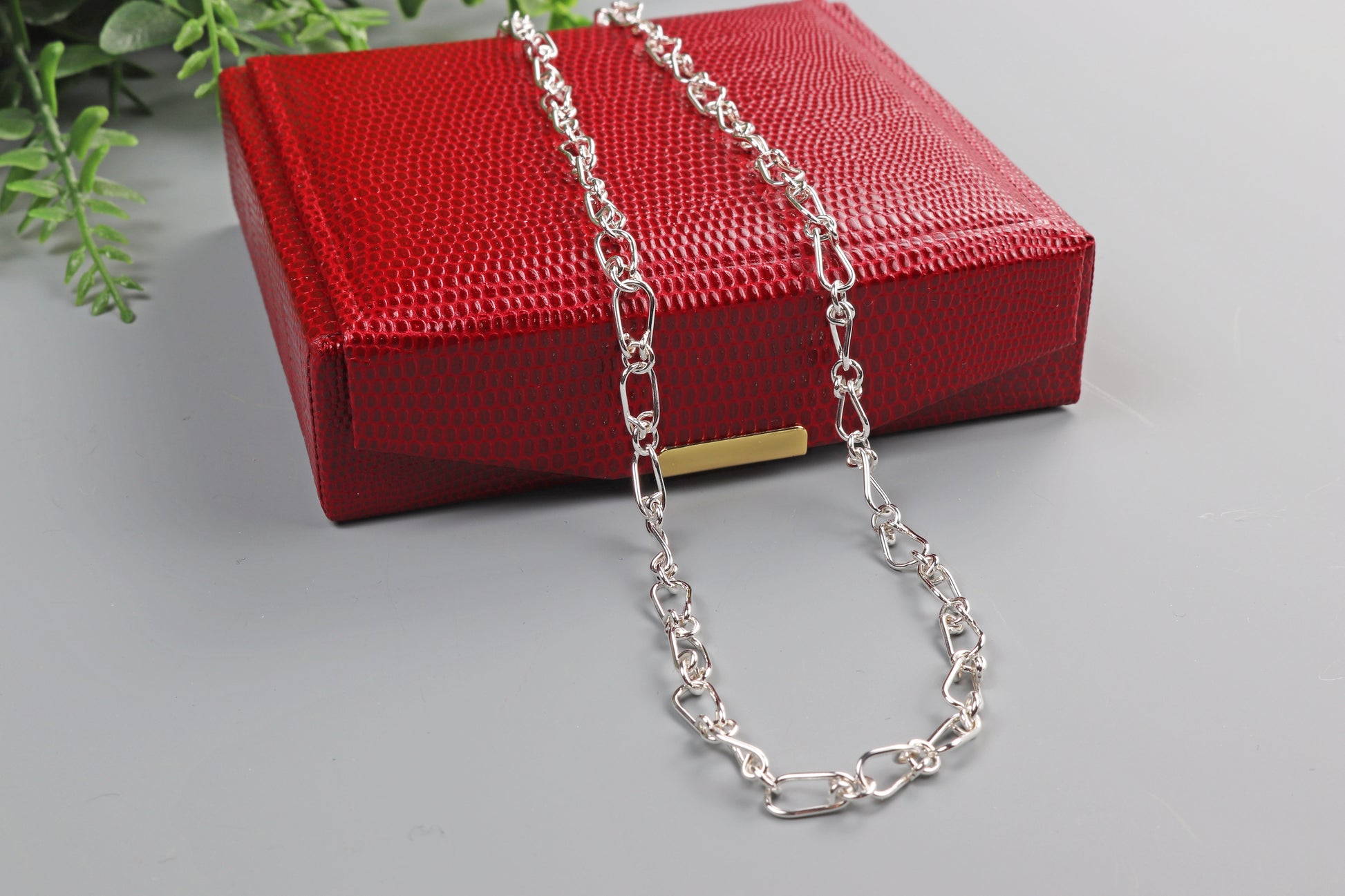 A red faux leather gift box is included with a handmade teardrop shaped link necklace. Shown on gray background.