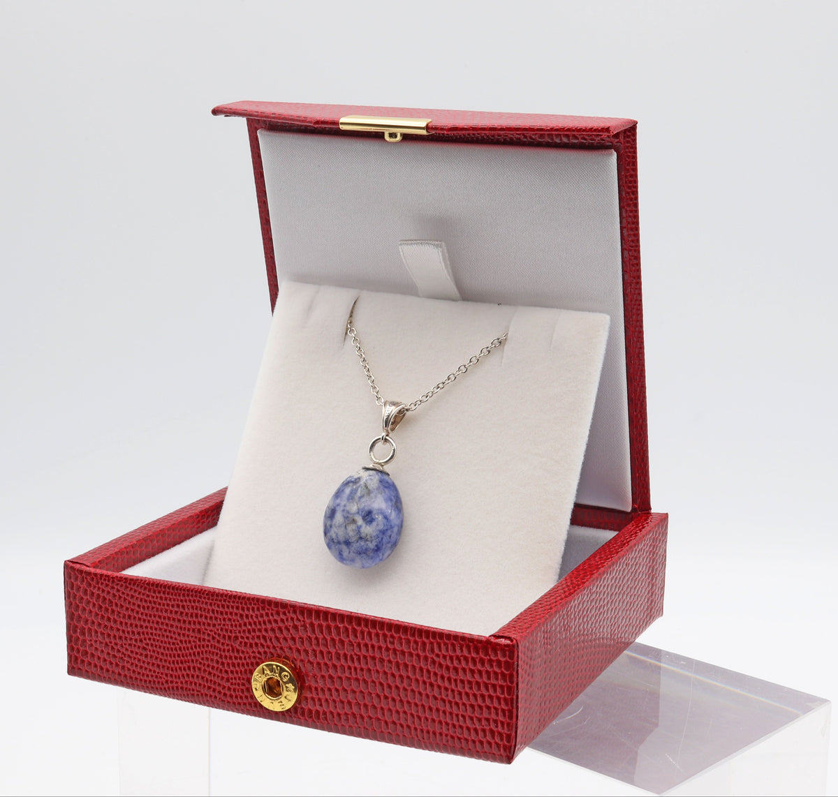 A silver necklace with a blue and white marbled pendant displayed inside an open red textured jewelry box on a white insert, set against a clean white background.