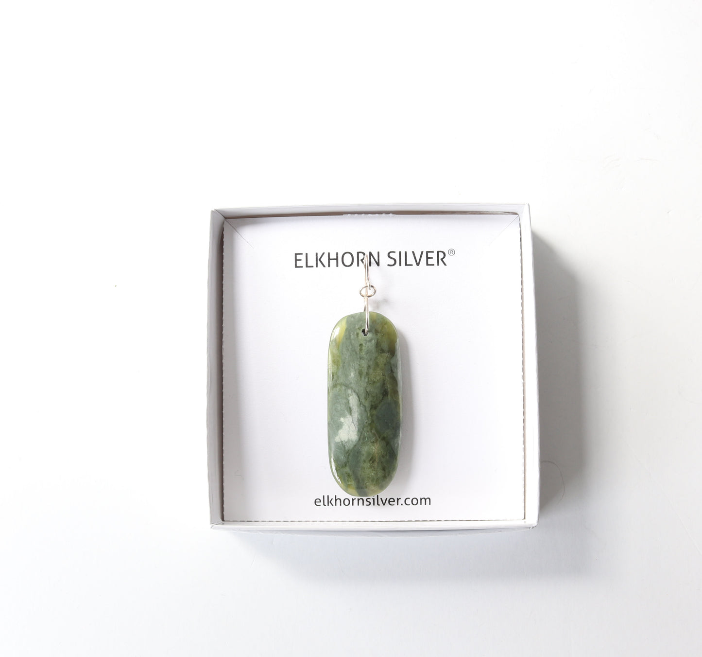 A green marbled california nephrite jade stone pendant with a Argentium silver infinity bow bail, displayed inside a white square gift box labeled 'ELKHORN SILVER'.
