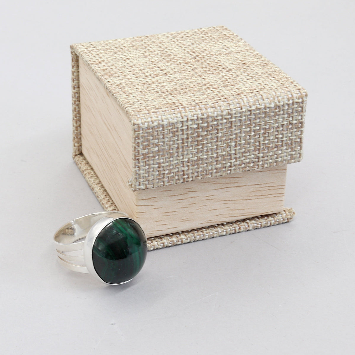 Handcrafted natural green Malachite ring with oval cabochon, polished fine silver bezel and solid Argentium 935 silver split-shank band.  Shown next to a canvas gift ring box against white background.