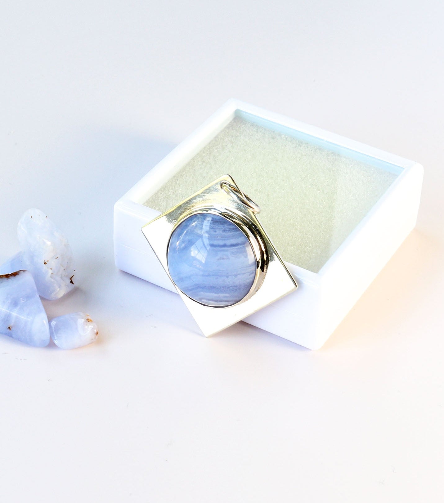 Blue Lace Agate pendant shown next to white gem box for storage or gift ready.  Raw Blue Lace agate pebbles are shown for props and not included.