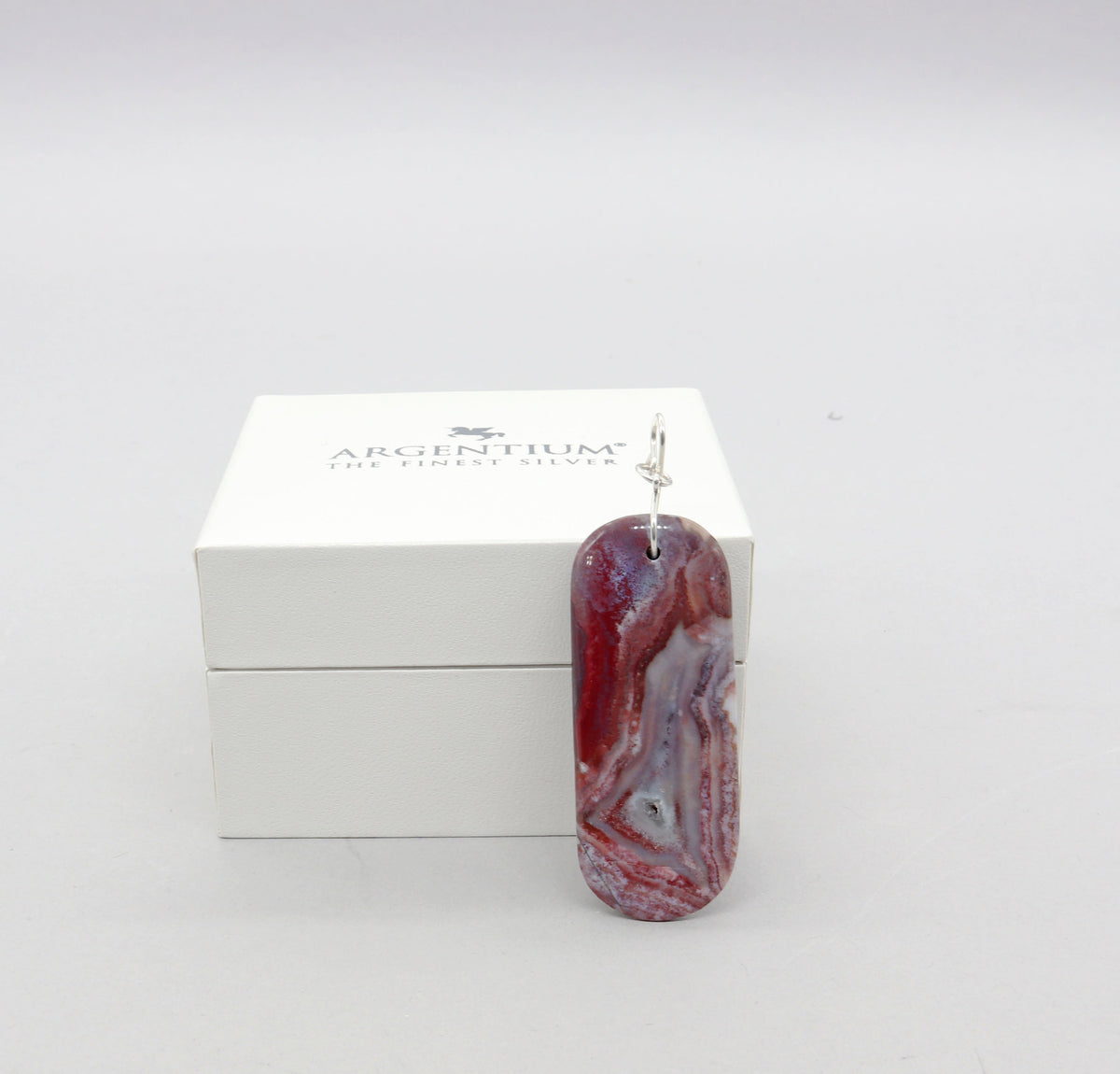  Handcrafted Red Mexico Agate pendant with mauve-gray and lavender hues, set in Argentium® 935 silver with a bow-shaped bail, presented in a white box labeled ‘ARGENTIUM – THE FINEST SILVER’.