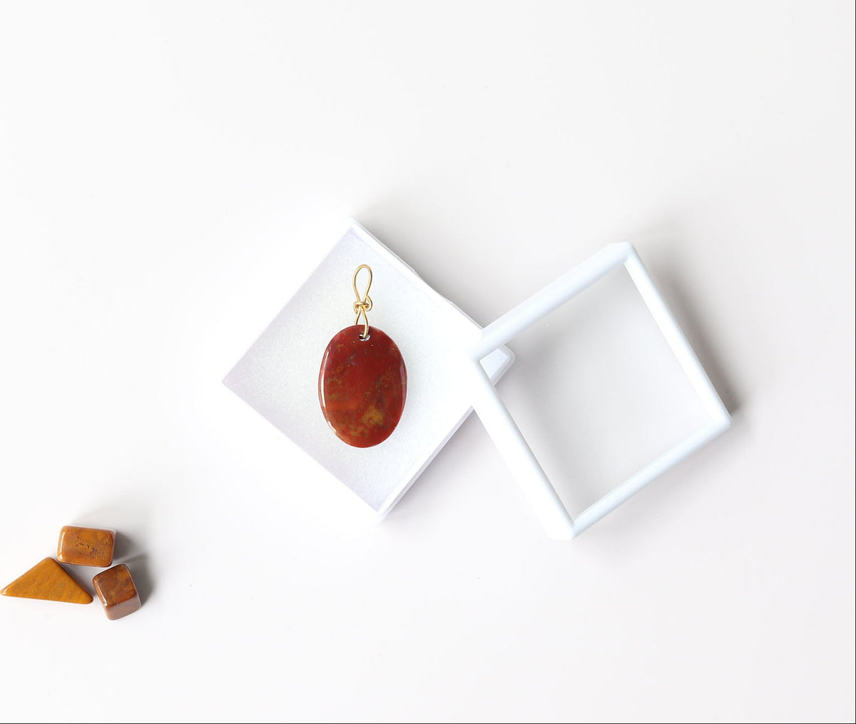 Sonoran Sunrise pendant shown in white gem box on white background with chips of sonoran sunrise as props shown on white background.