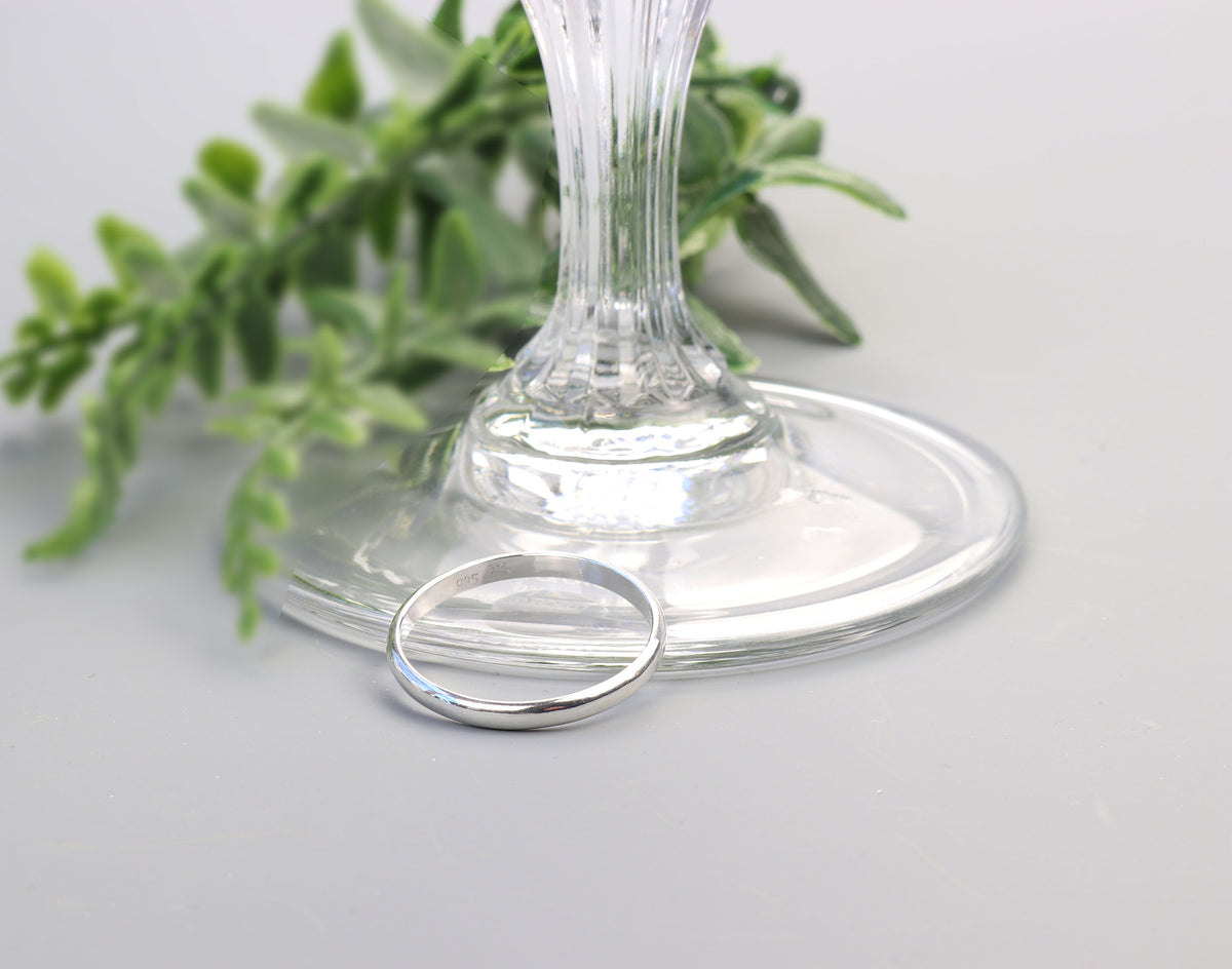 Handcrafted solid Argentium 935 silver half-round ring with smooth polished band displayed beside a clear glass pedestal.