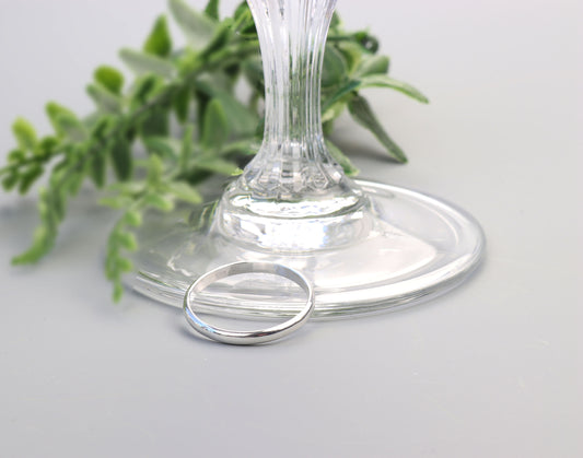 Handcrafted solid Argentium 935 silver half-round ring with smooth polished band displayed beside a clear glass pedestal.