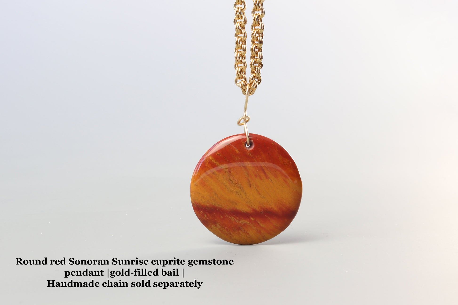 Round red Sonoran Sunrise eugrite gemstone pendant on a gold chain against a white background.