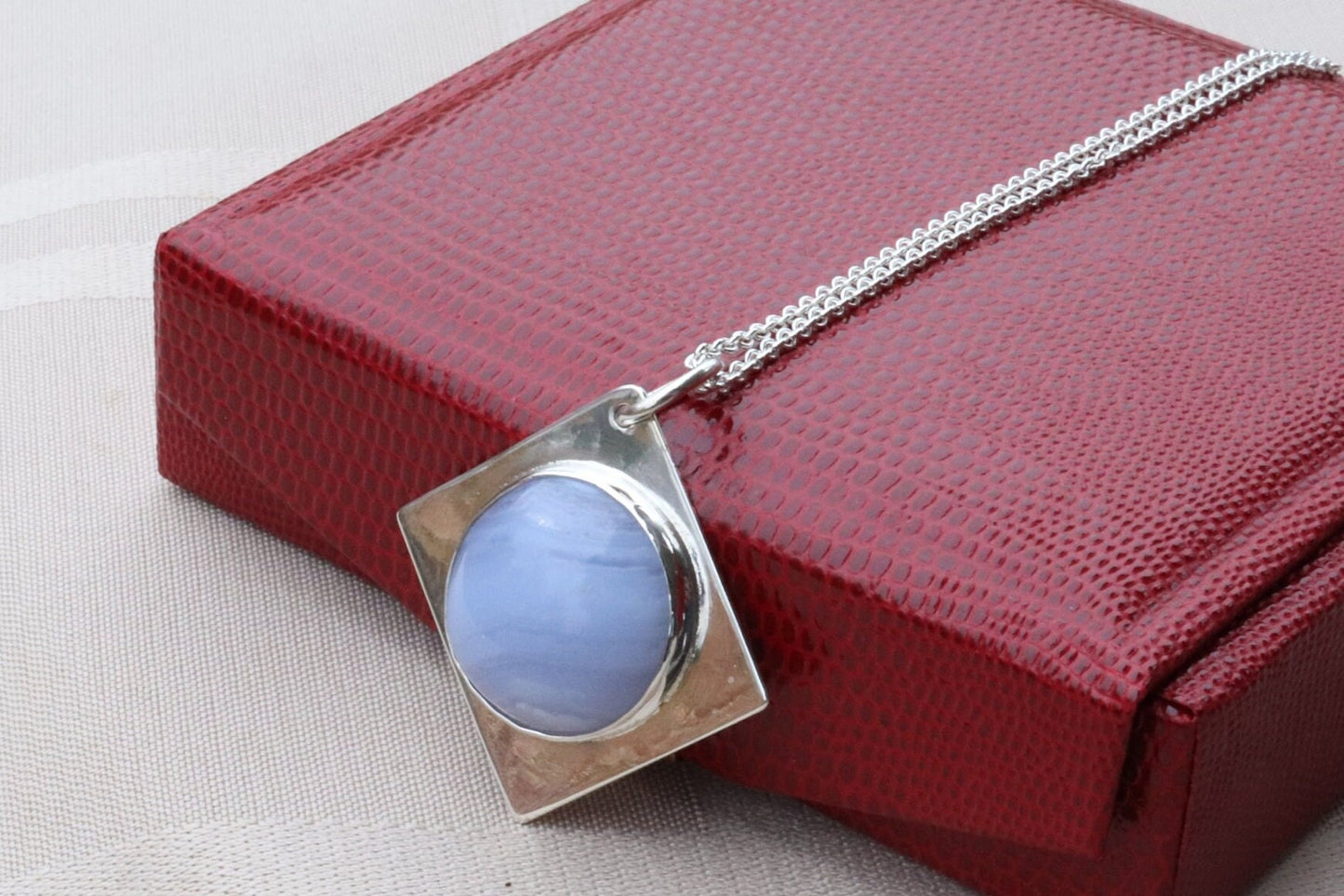 An authentic, high-quality Blue Lace Agate Cabochon, handcrafted in our Missouri USA studio and set within a custom four-point diamond shaped sterling Argentium 935 Silver, and to complete the look a complementary 18" premium silver chain is included. Ready to gift in a red faux leather gift box.