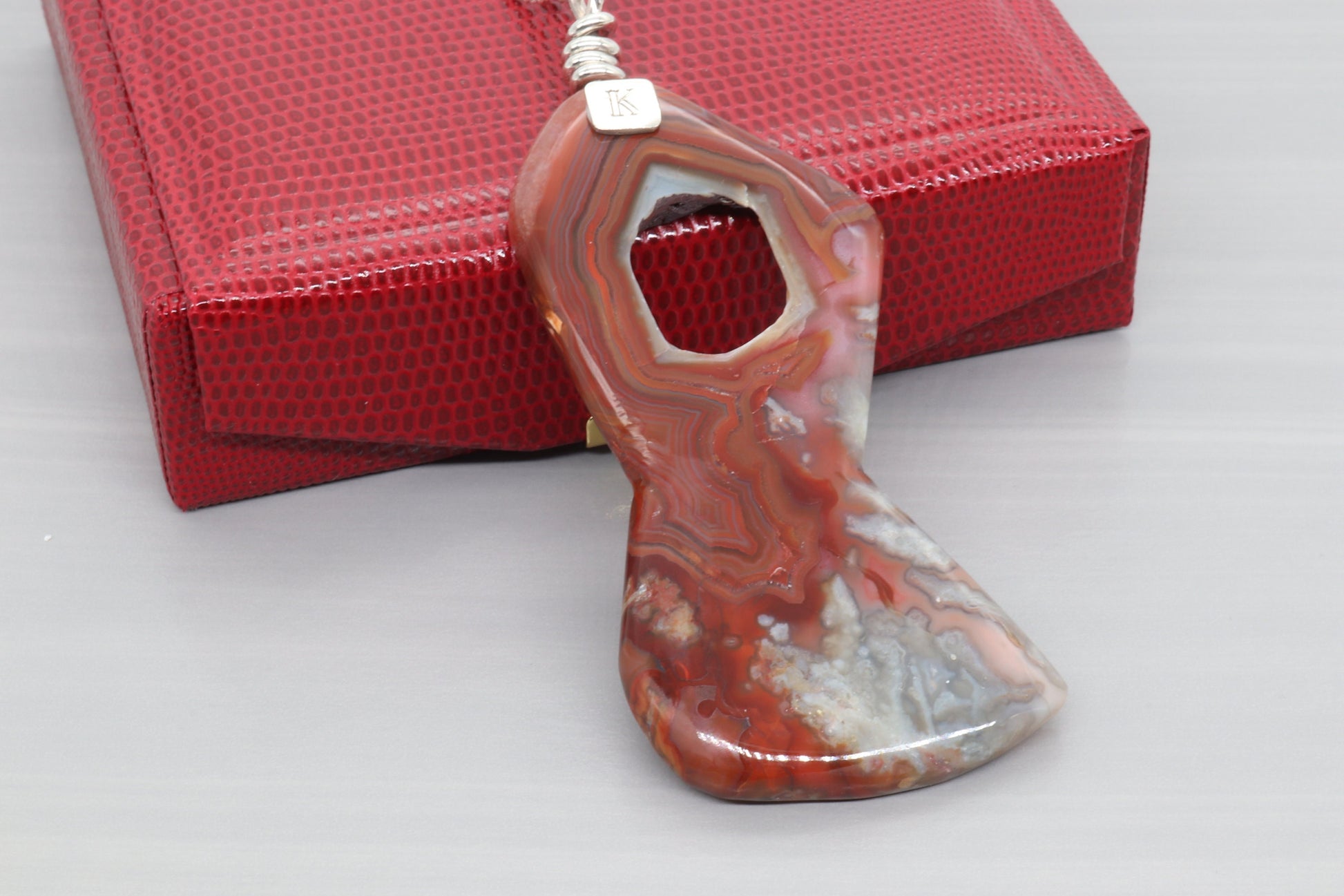 A natural 3.5 inch Crazy Lace Agate Gemstone pendant necklace showcases the mesmerizing beauty of nature's art. Handcut and freeform polished to showcase the unique swirling patterns and vibrant reds, pink and gray hues of the Crazy Lace Agate gemstone.  Ready to gift in a red faux leather gift box.