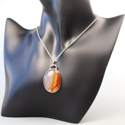 A Carnelian gemstone was selected for its glassy luster, unique variation of semi-translucent grays and rich deep orange hues. In our Missouri studio, we hand-cut and polished this into a cabochon shape and set in a handcrafted sterling silver Argentium 935 bezel paired with a complementary Argentium silver chain. The Carnelian has been used for centuries in jewelry, amulets and seal making it a timeless and versatile statement piece.