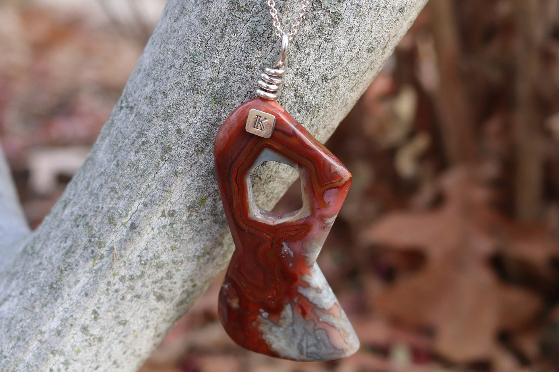 A natural 3.5 inch Crazy Lace Agate Gemstone pendant necklace showcases the mesmerizing beauty of nature's art. Handcut and freeform polished to showcase the unique swirling patterns and vibrant reds, pink and gray hues of the Crazy Lace Agate gemstone.