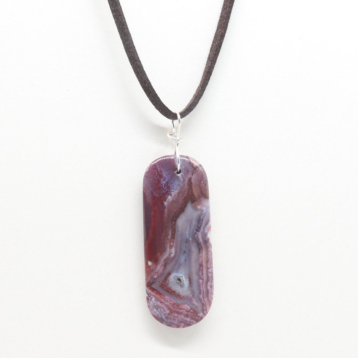 A one-of-a-kind Red Mexico Agate pendant with hues of mauve gray and deep lavender. Hand-cut and expertly freeform polished to accentuate the charming small crystal feature and stunning translucent patterns. This stunning piece features an original infinity bow wire bail made from sterling Argentium 935 silver, renowned for its elevated silver content, exceptional resistance to tarnish, and enduring brilliance.