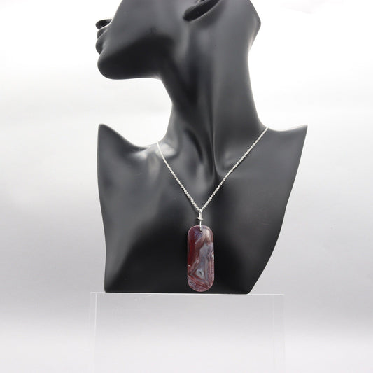 A one-of-a-kind Red Mexico Agate pendant with hues of mauve gray and deep lavender. Hand-cut and expertly freeform polished to accentuate the charming small crystal feature and stunning translucent patterns. This stunning piece features an original infinity bow wire bail made from sterling Argentium 935 silver, renowned for its elevated silver content, exceptional resistance to tarnish, and enduring brilliance.