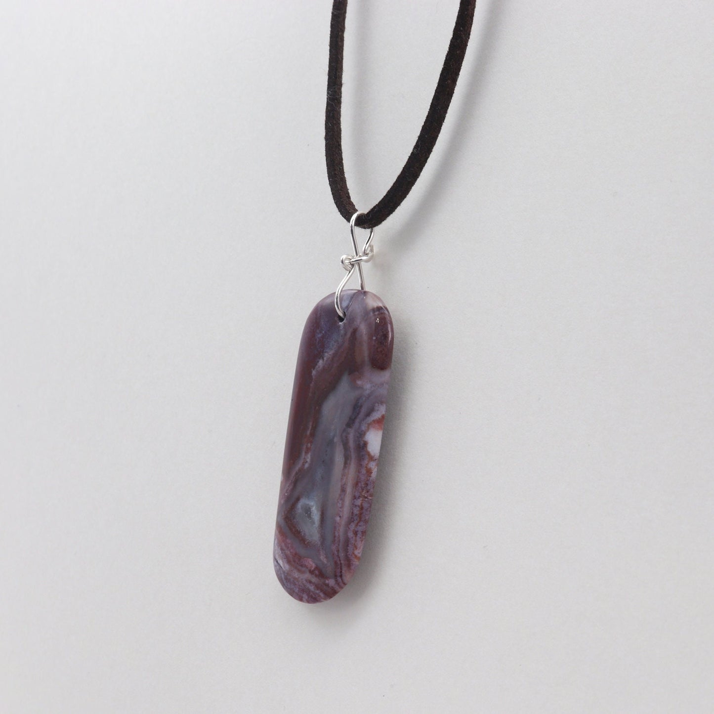 A one-of-a-kind Red Mexico Agate pendant with hues of mauve gray and deep lavender. Hand-cut and expertly freeform polished to accentuate the charming small crystal feature and stunning translucent patterns. This stunning piece features an original infinity bow wire bail made from sterling Argentium 935 silver, renowned for its elevated silver content, exceptional resistance to tarnish, and enduring brilliance.