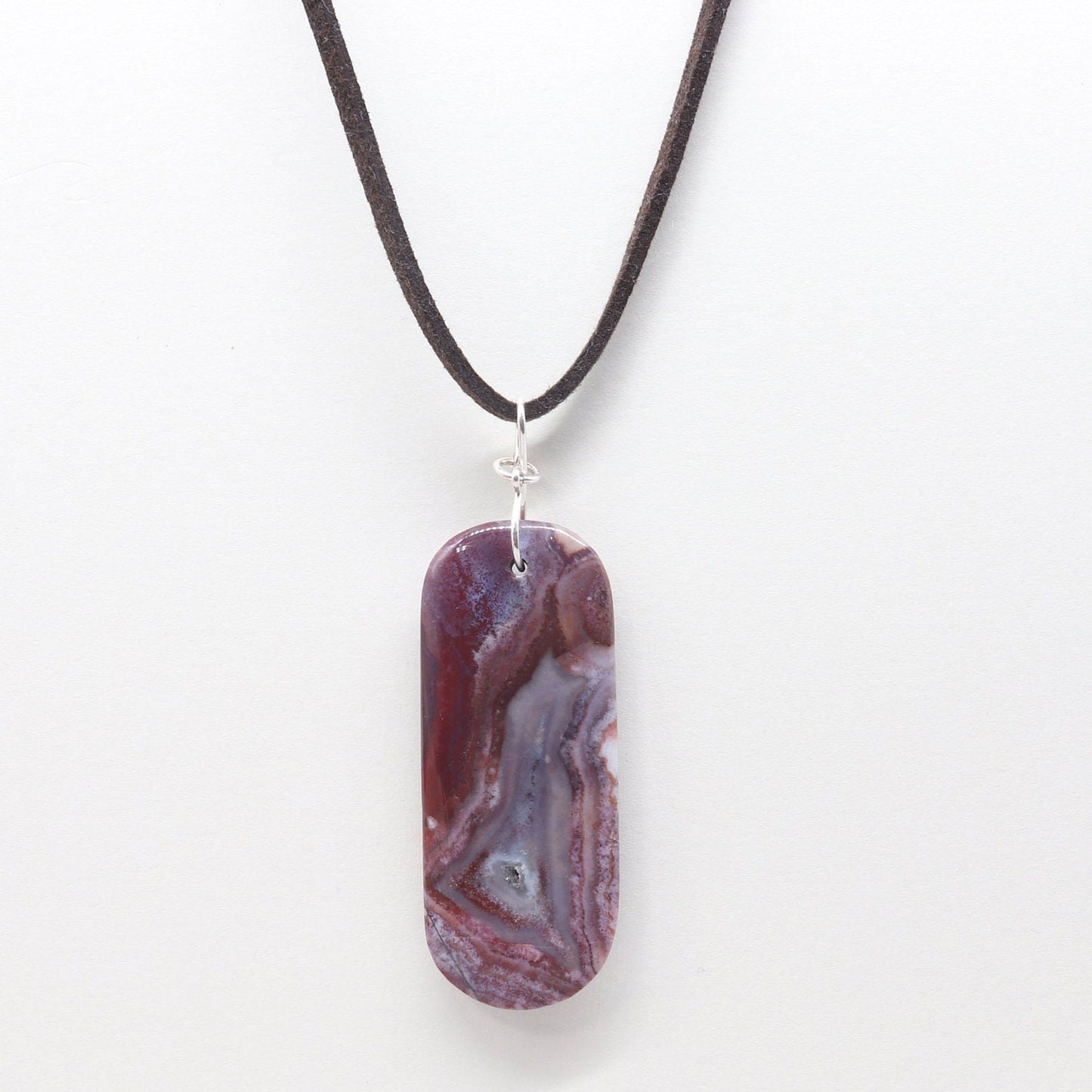 A one-of-a-kind Red Mexico Agate pendant with hues of mauve gray and deep lavender. Hand-cut and expertly freeform polished to accentuate the charming small crystal feature and stunning translucent patterns. This stunning piece features an original infinity bow wire bail made from sterling Argentium 935 silver, renowned for its elevated silver content, exceptional resistance to tarnish, and enduring brilliance.