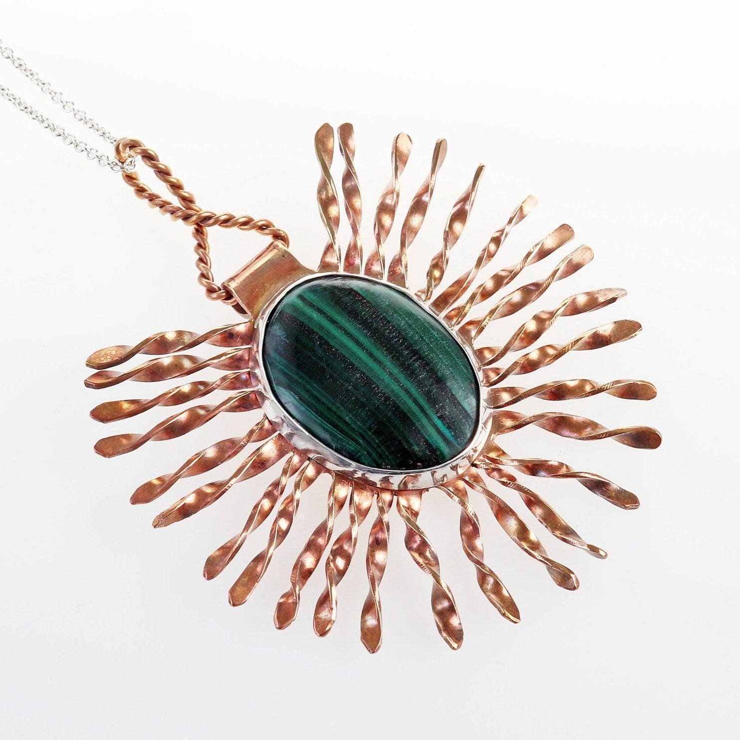 A unique Malachite Gemstone Pendant handcrafted in our studio. The Malachite gemstone has been handcut and polished into a cabochon and encased in a sterling 935 Argentium silver setting. A unique starburst pattern in Jewelers Brass with a captivating copper patina, elegantly encircles the polished malachite stone. Plus to complete the look a complementary sterling 935 Argentium silver chain is included.