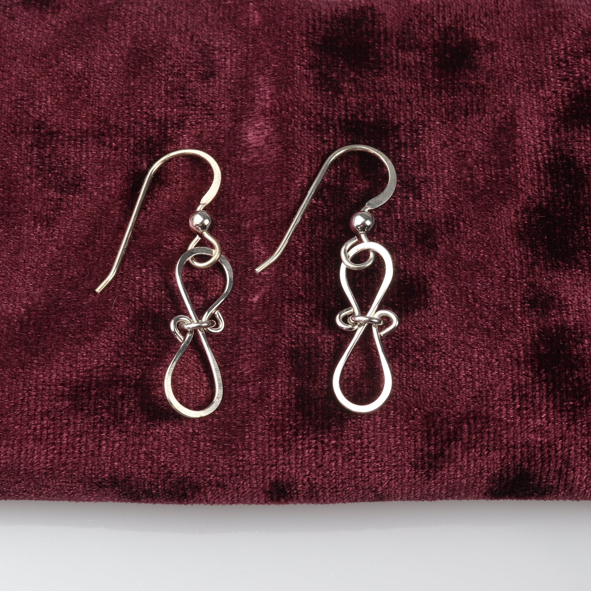 A pair of Silver Bow Earrings in solid premium 935 Argentium silver,with a hammered finish shown against burgundy velvet