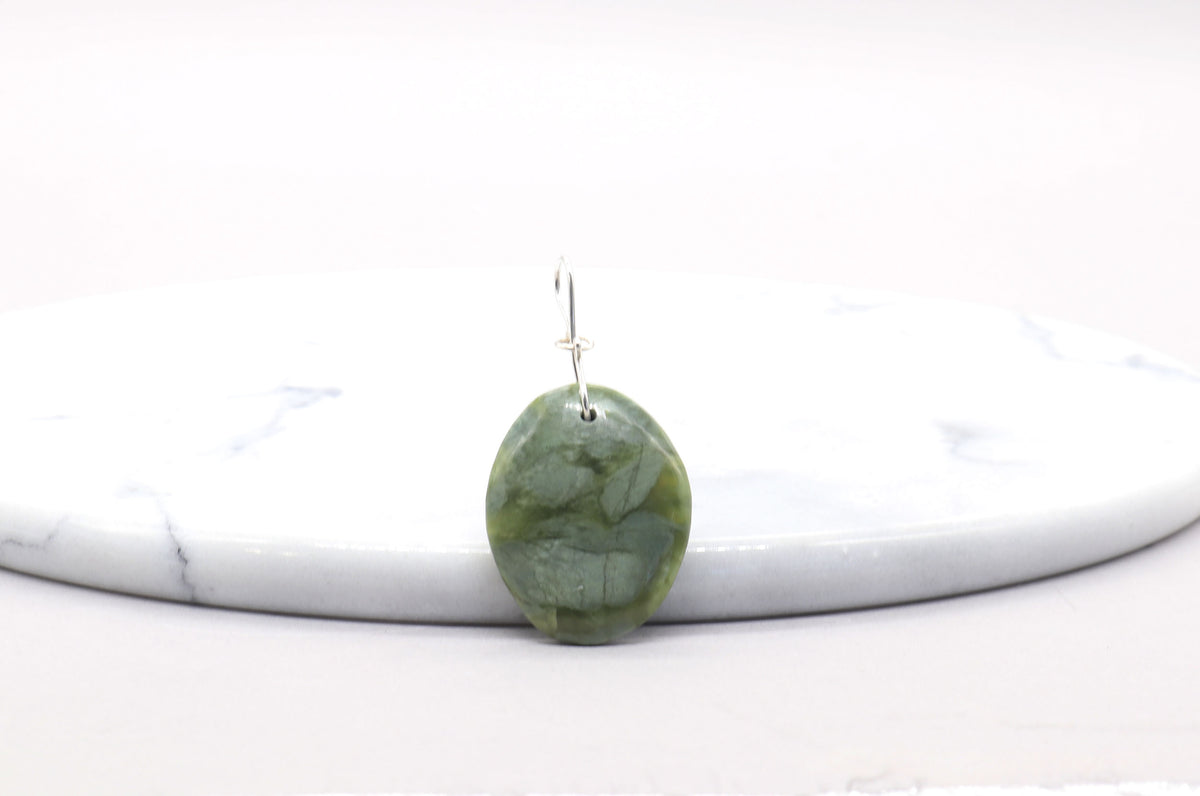 A single green jade stone pendant with Argentium custom silver wire bail, resting on a white marble tray against a white background.