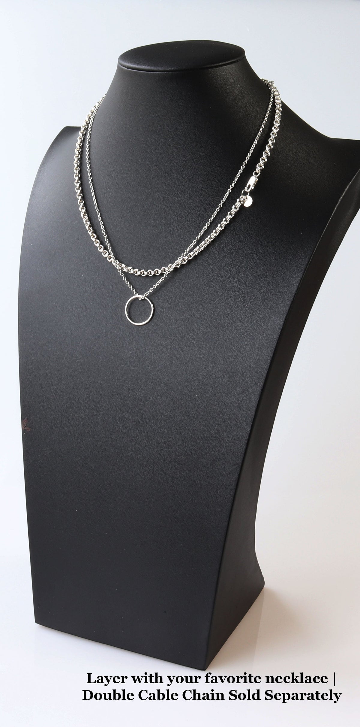 A silver double cable chain necklace with a small ring pendant, displayed on a black jewelry bust. Text at the bottom reads 'Layer with your favorite necklace | Double Cable Chain Sold Separately'.