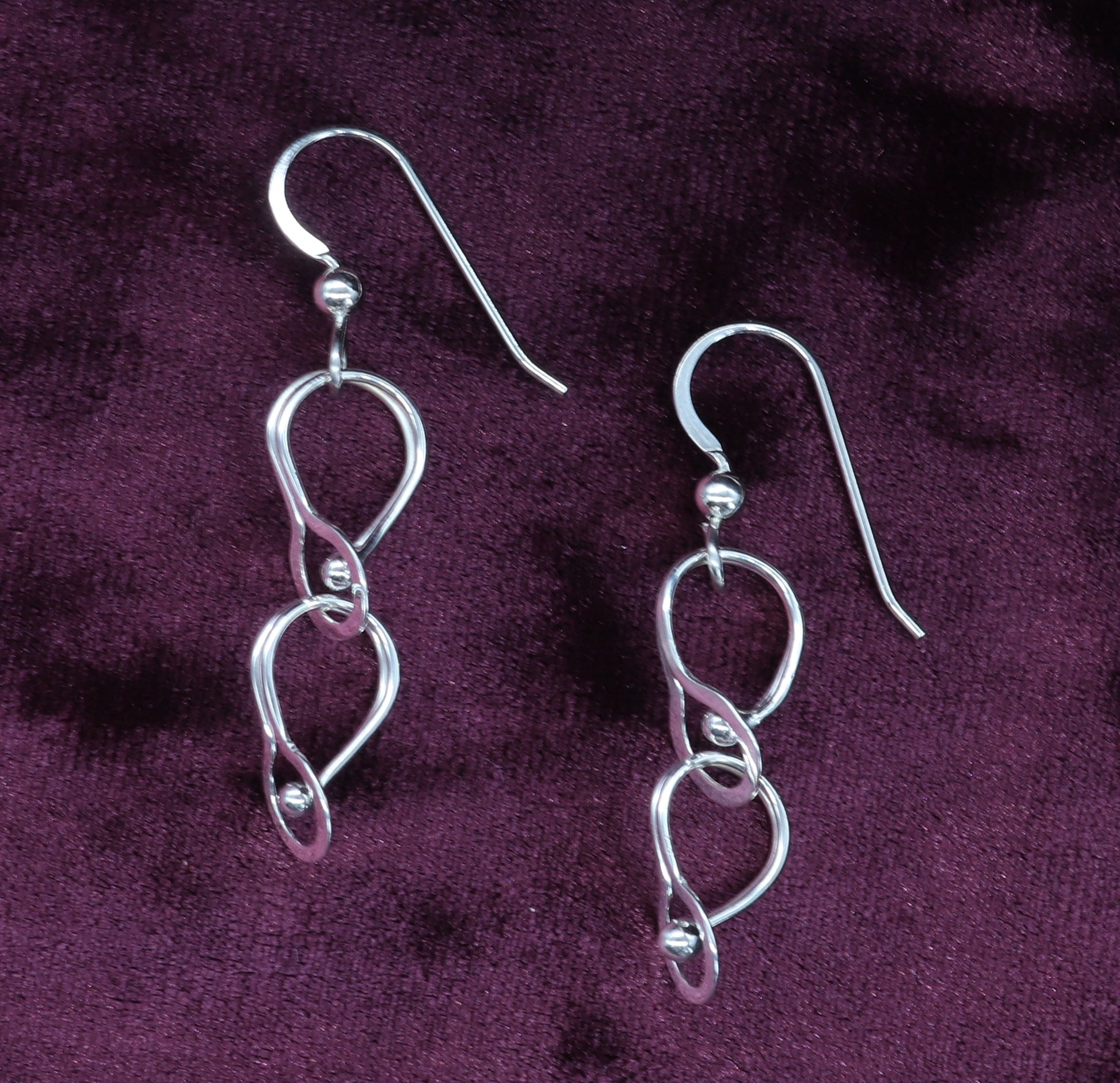 Argentium loop dangle earrings shown on burgundy velvet background