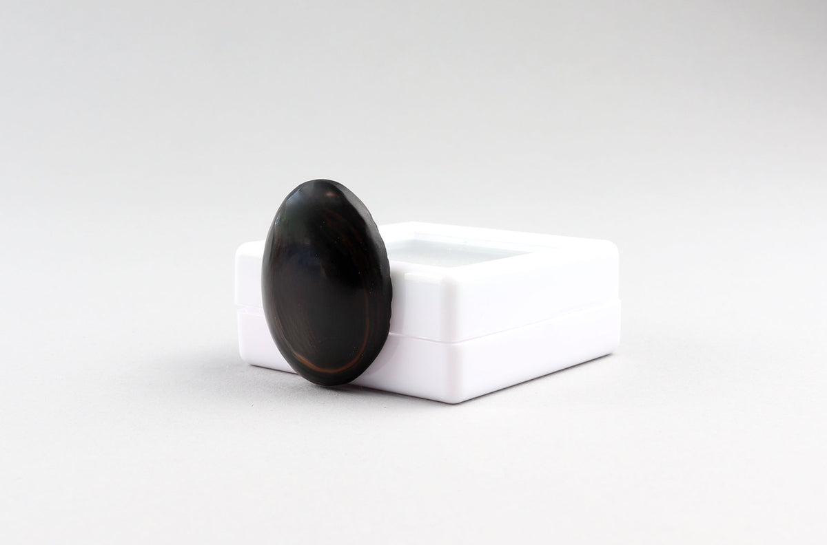 Angled side view of hand-cut Mahogany Obsidian cabochon showing its rounded profile shown against light gray background.