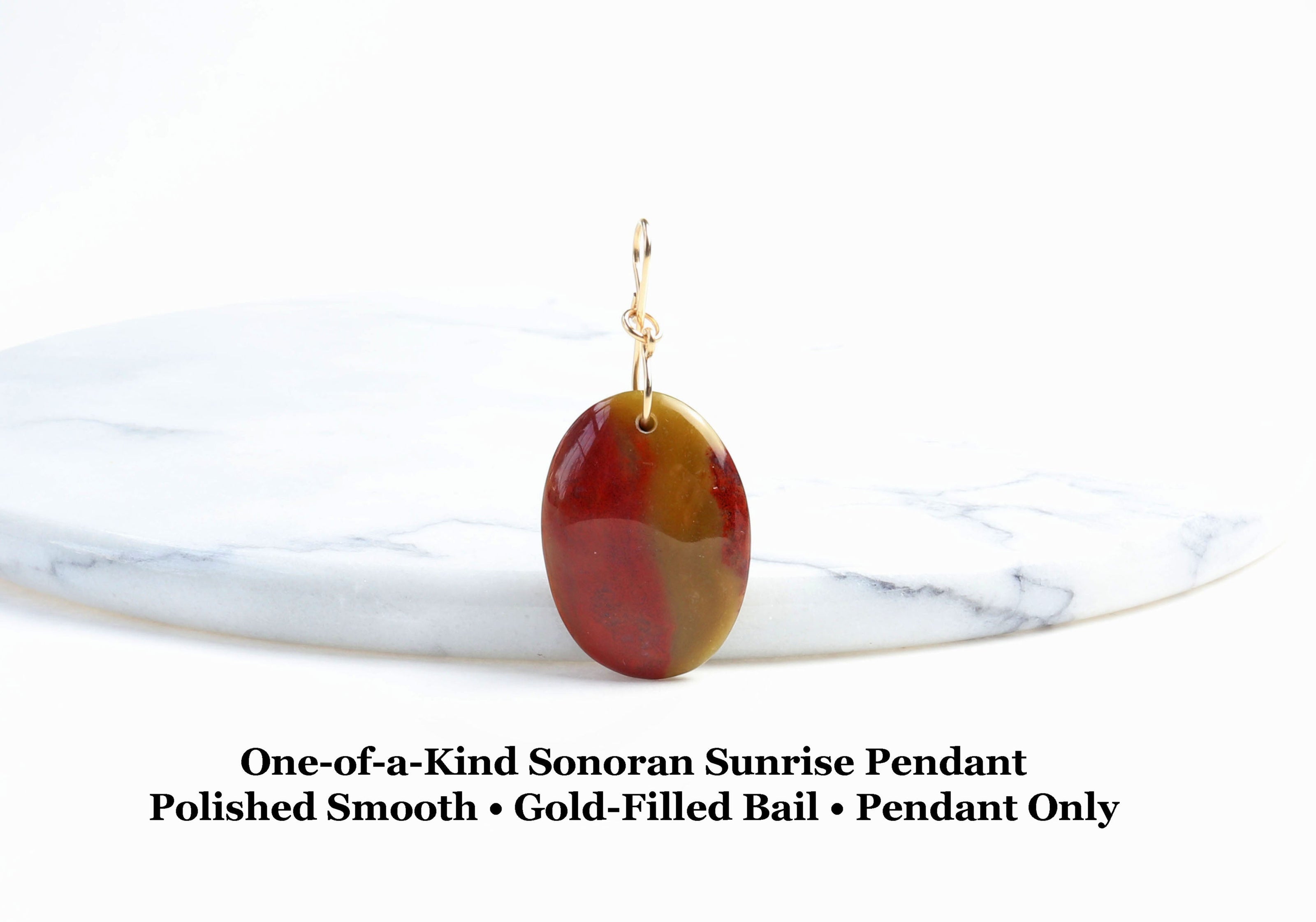 Sonoran Sunrise pendant with deep red cuprite, ochre, and chartreuse tones, displayed upright with a gold-filled bail on a white marble background.