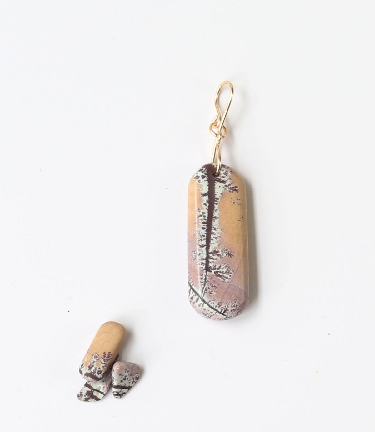 Natural Sonoran Dendritic Rhyolite | Gold Filled Custom Bail. This one-of-a-kind Sonoran Dendritic Rhyolite pendant is hand-cut and polished in our Missouri studio, revealing soft pink, tan, and deep brown tones with delicate dendritic patterns formed naturally over time. Shown on white background next to small pebbles of rhyolite used for props.
