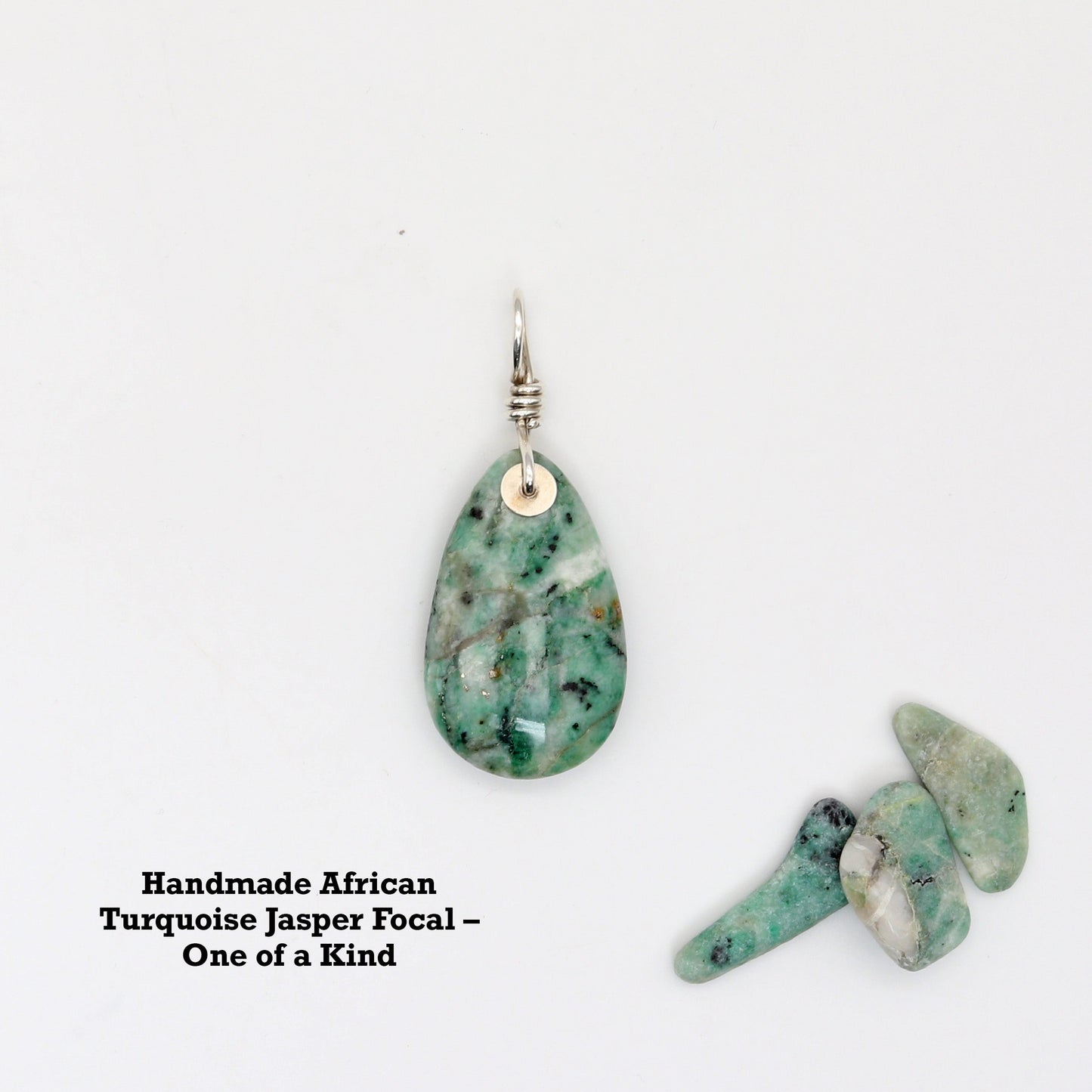 striking African Turquoise pendant, hand-cut and polished on both sides to highlight its rich blend of blue-green hues. Each stone is completely unique, offering natural patterns that resemble traditional turquoise but with its own earthy charm.  Shown against white background with small African Turquoise pebbles for props and text overlay Handmade African Turquoise Jasper Focal One of a Kind