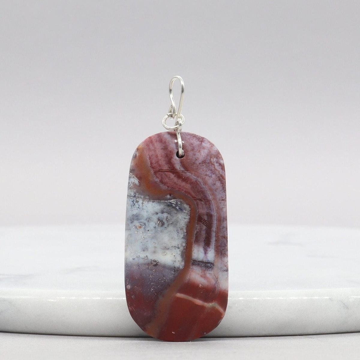 Red Mexican Agate pendant with Argentium Silver bail on white marble against gray background