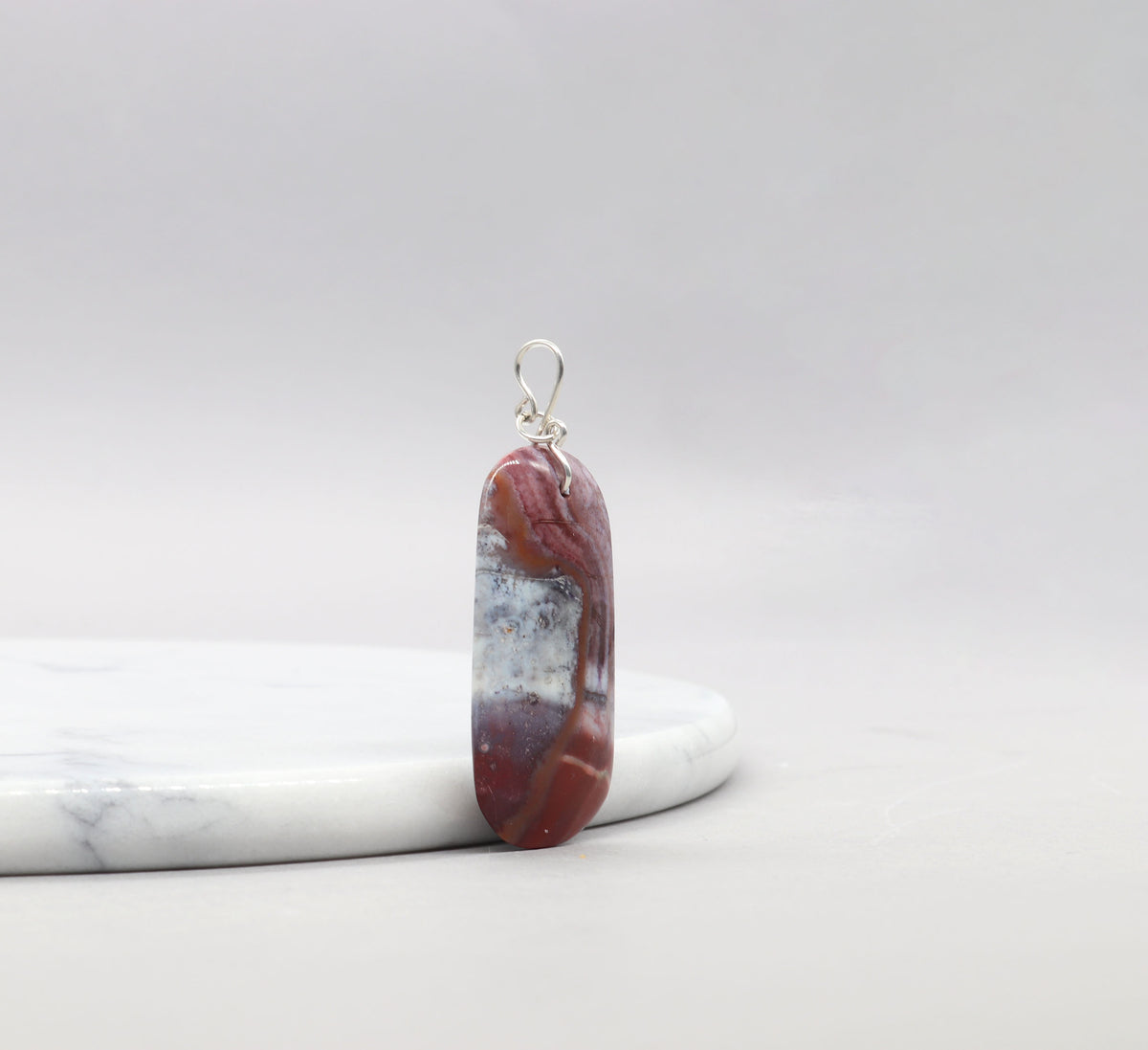 Red Mexican Agate pendant with Argentium Silver bail  shown at left angle on white marble against gray background