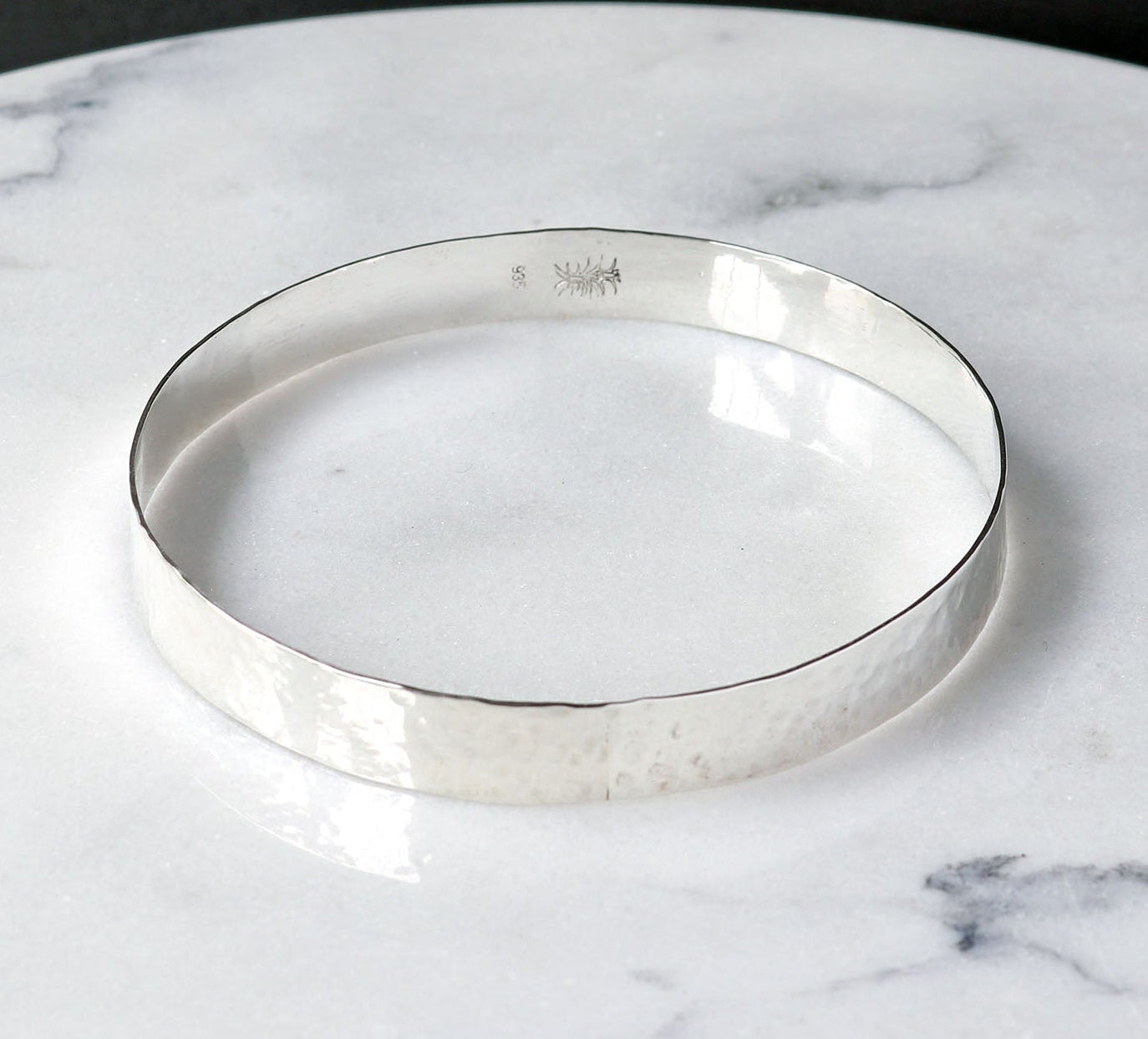 Argentium Silver Bangle shown on white marble with black background.