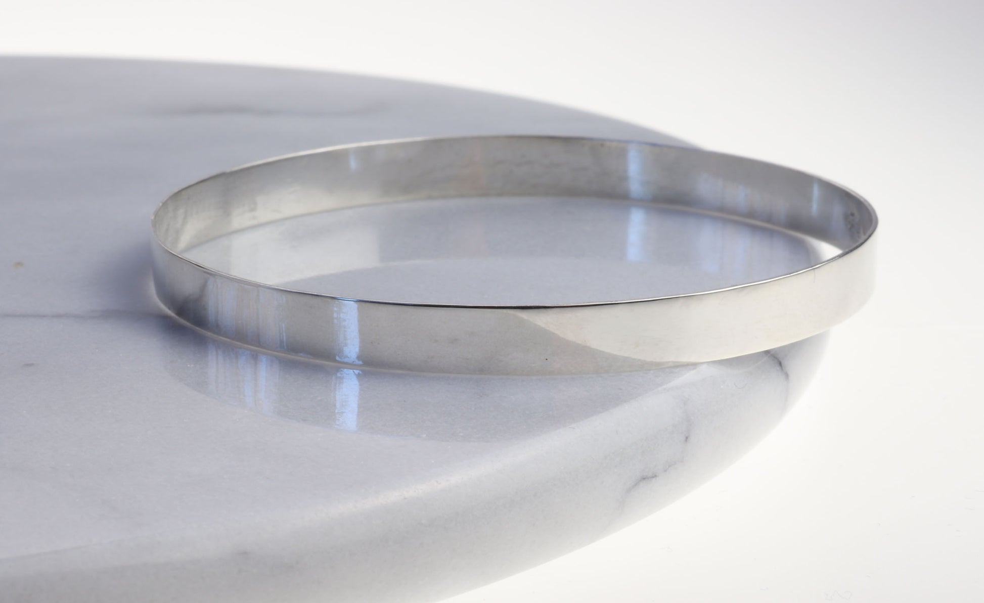 A side view of a high polish Flat Bangle Bracelet in tarnish resistant and hypoallergenic Argentium® 935 silver.  Pair with other bracelets for that modern and sophisticated look.
Shown on marble background.