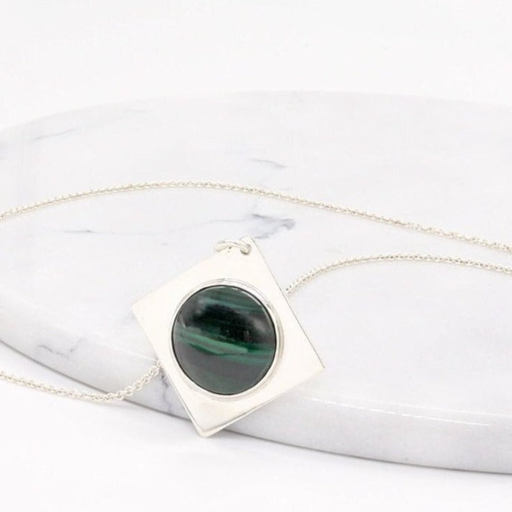 Handcrafted malachite pendant necklace in Argentium silver with geometric setting shown against white marble slab against a white background.