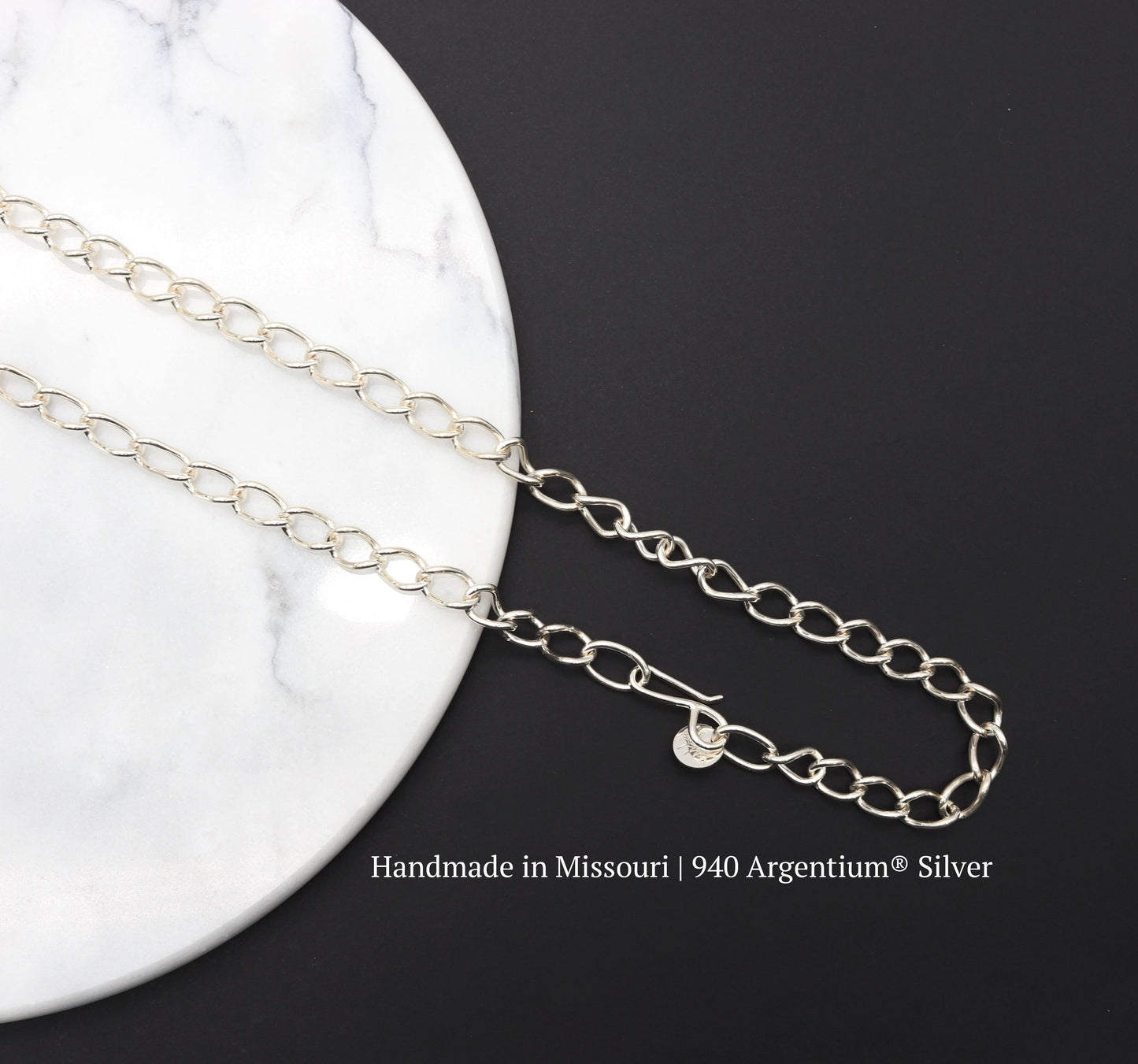 A hand-forged oval link chain necklace. Crafted from solid Argentium® 940 silver in our Missouri studio, Shown on a black background over a white round marble slab.