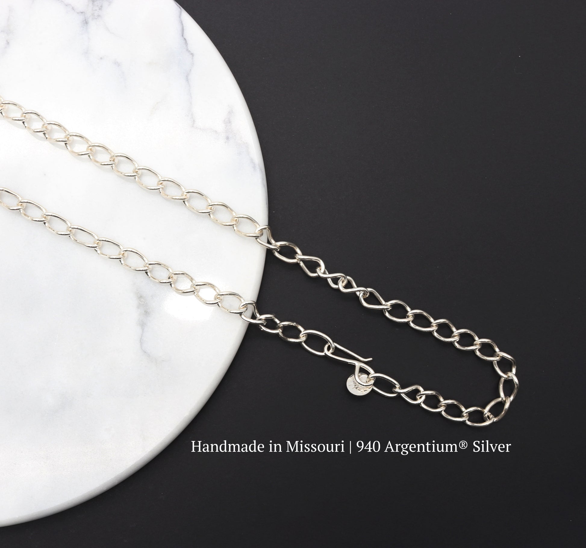 A hand-forged oval link chain necklace. Crafted from solid Argentium® 940 silver in our Missouri studio, Shown on a black background over a white round marble slab.
