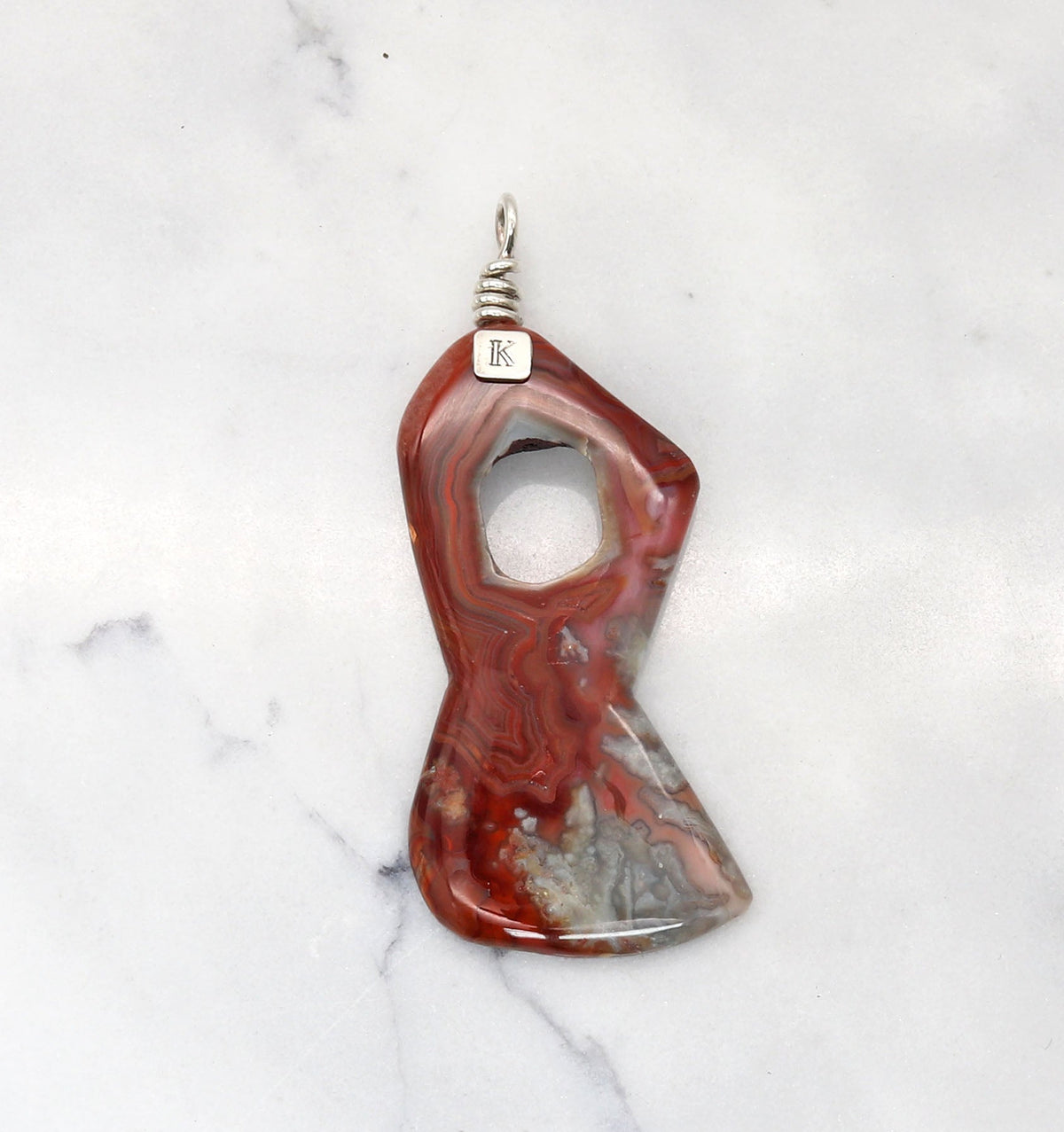 One-of-a-kind Crazy Lace Agate pendant with open center and Argentium Silver bail shown on a white marble slab background.