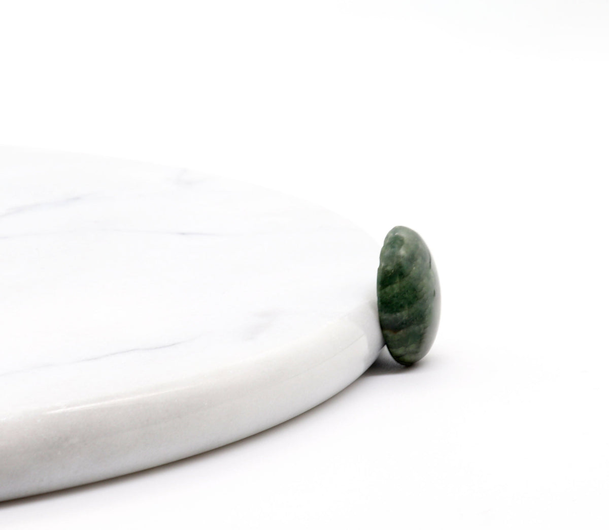 A sideview of this handcut and polished Arizona Green Lizard gemstone cabochon stone resting on the edge of a white marble serving board against a clean white background.