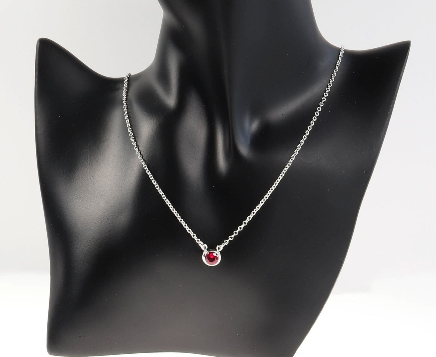6mm lab ruby necklace in Argentium silver shown on black resin jewelry form against light gray background.