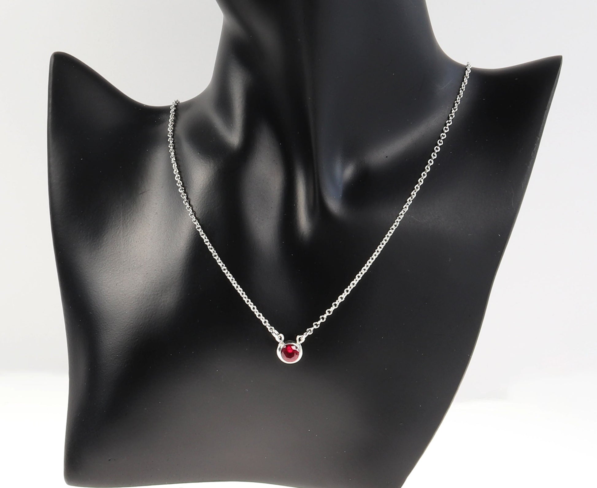 6mm lab ruby necklace in Argentium silver shown on black resin jewelry form against light gray background.