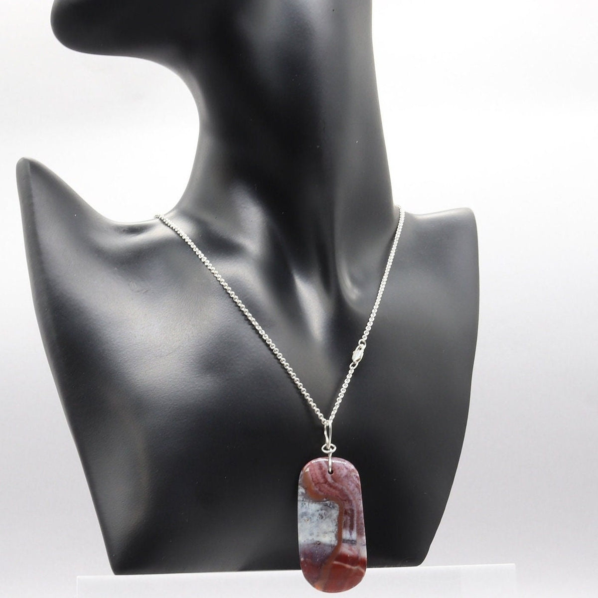 Red Mexican Agate pendant with Argentium Silver bail and Argentium necklace displayed on black resin jewelry form on white marble against gray background