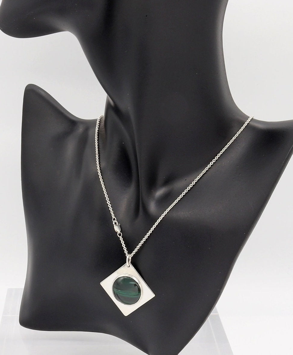 Handcrafted malachite pendant necklace in Argentium silver with geometric setting shown on black resin model on white marble slab against a white background.