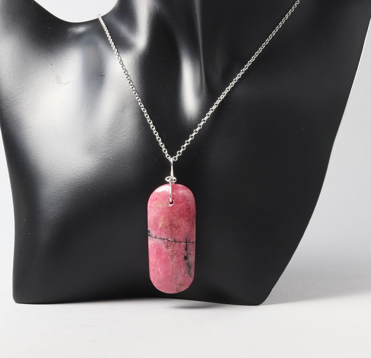 An silver chain necklace with a polished pink stone pendant featuring natural dark veining, displayed on a black mannequin bust against a light gray background.