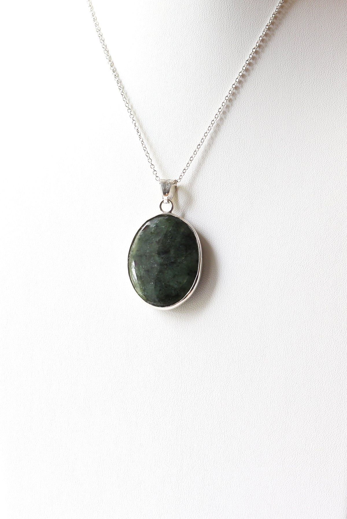 An Argentium silver chain necklace with an oval Wyoming Jade green stone pendant, displayed on a white jewelry form background.