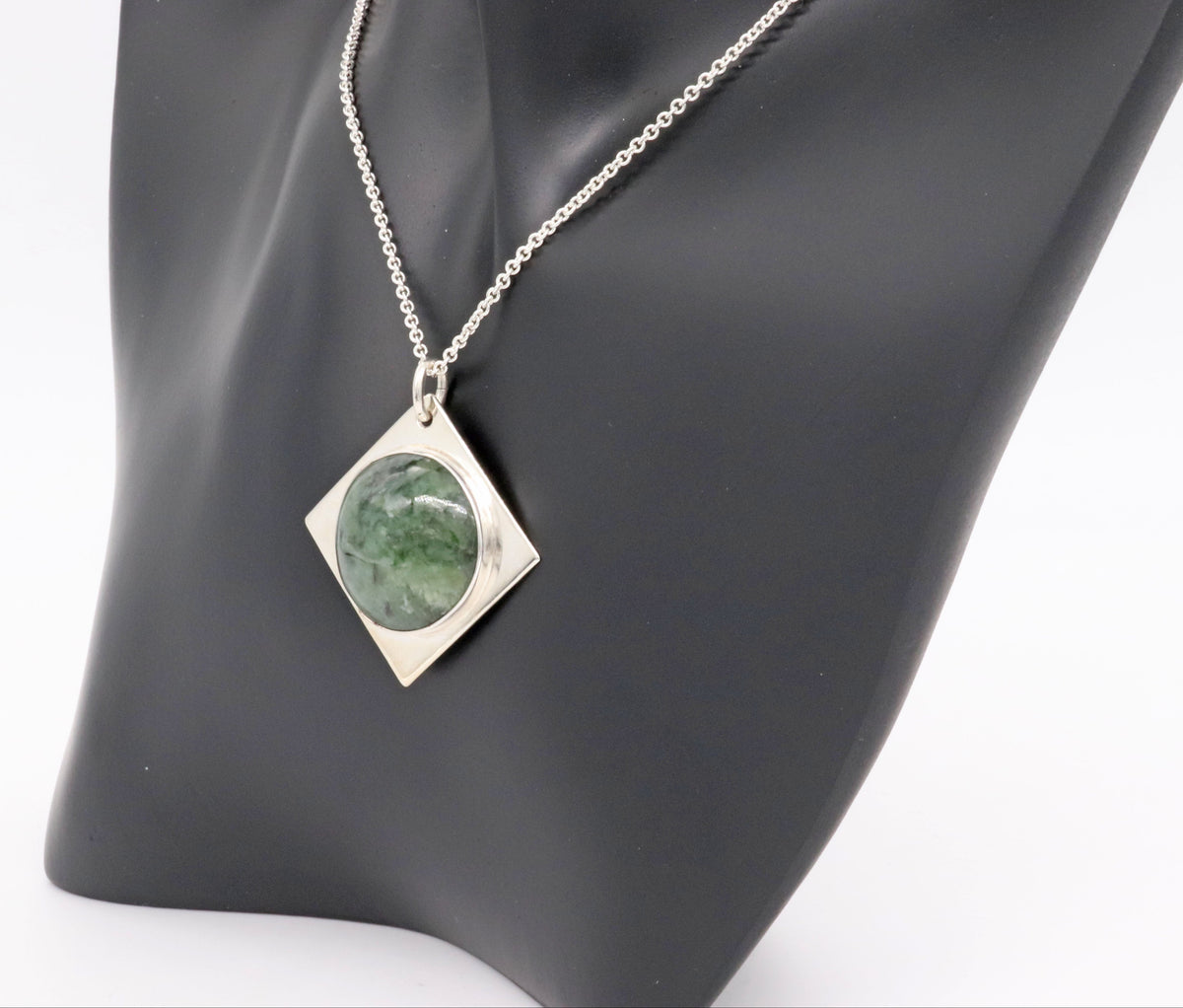 Wyoming Jade cabochon stone set in solid Argentium silver paired with Argentium silver 1.7 chain. Shown on black resin jewelry form against white background.